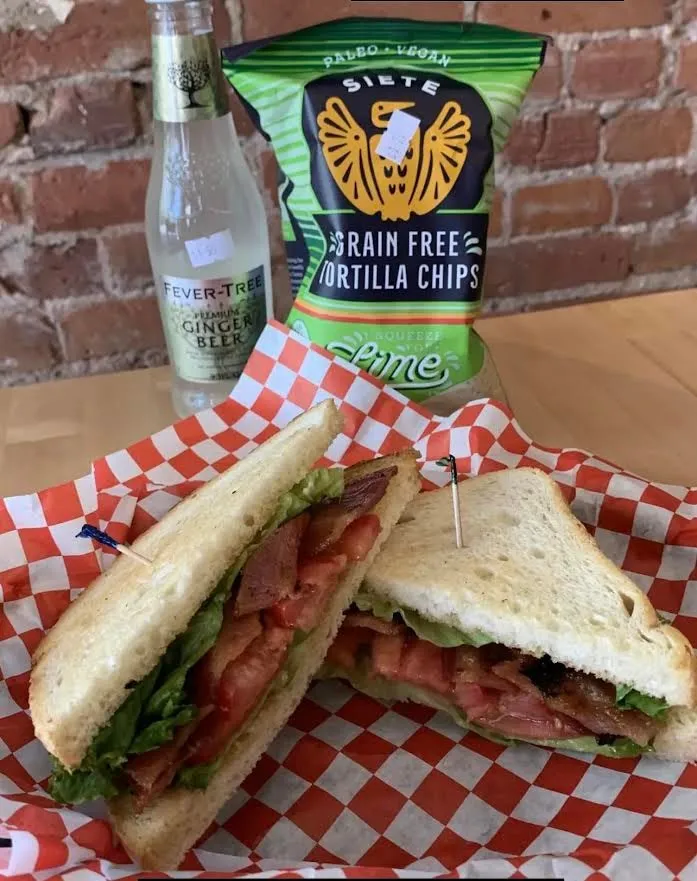 BLT sandwich with tortilla chips and ginger beer on a brick-wall table