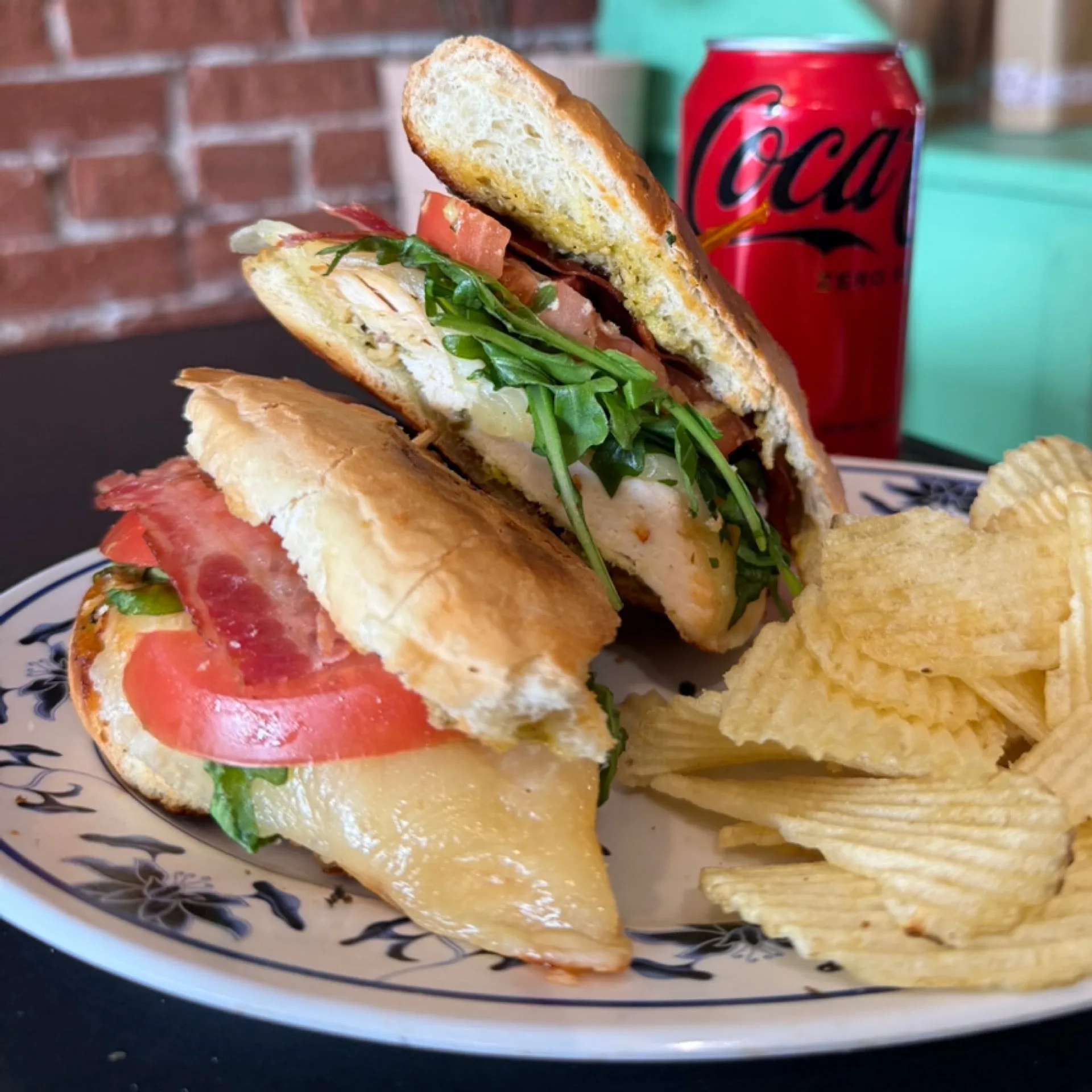 Chicken croissant sandwich with tomato, arugula, and bacon, served with chips