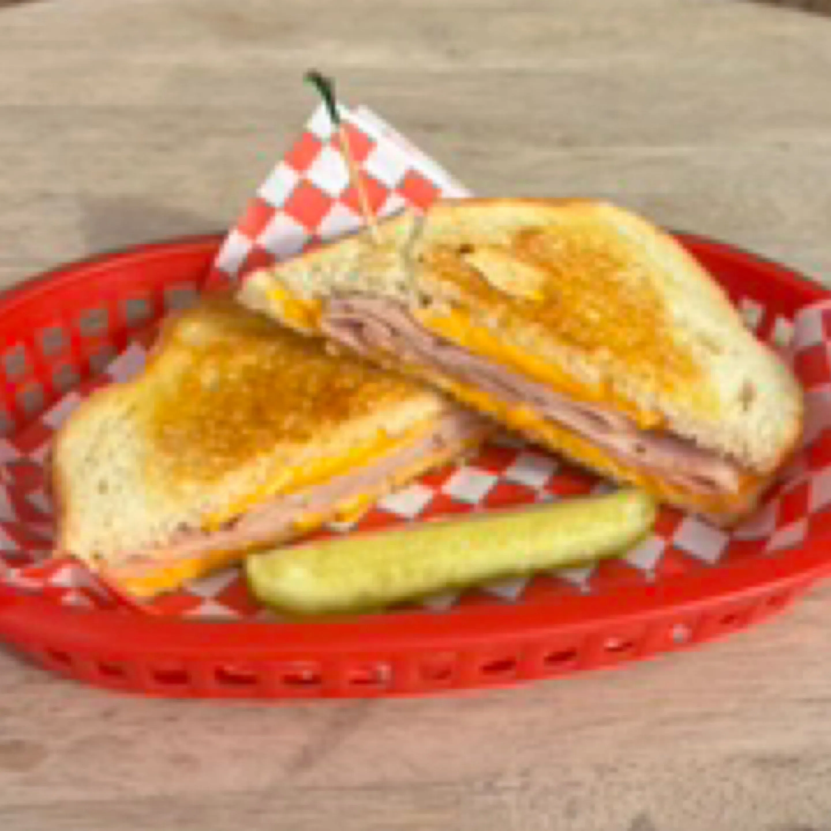 Grilled ham and cheese sandwich with a pickle in a red deli basket