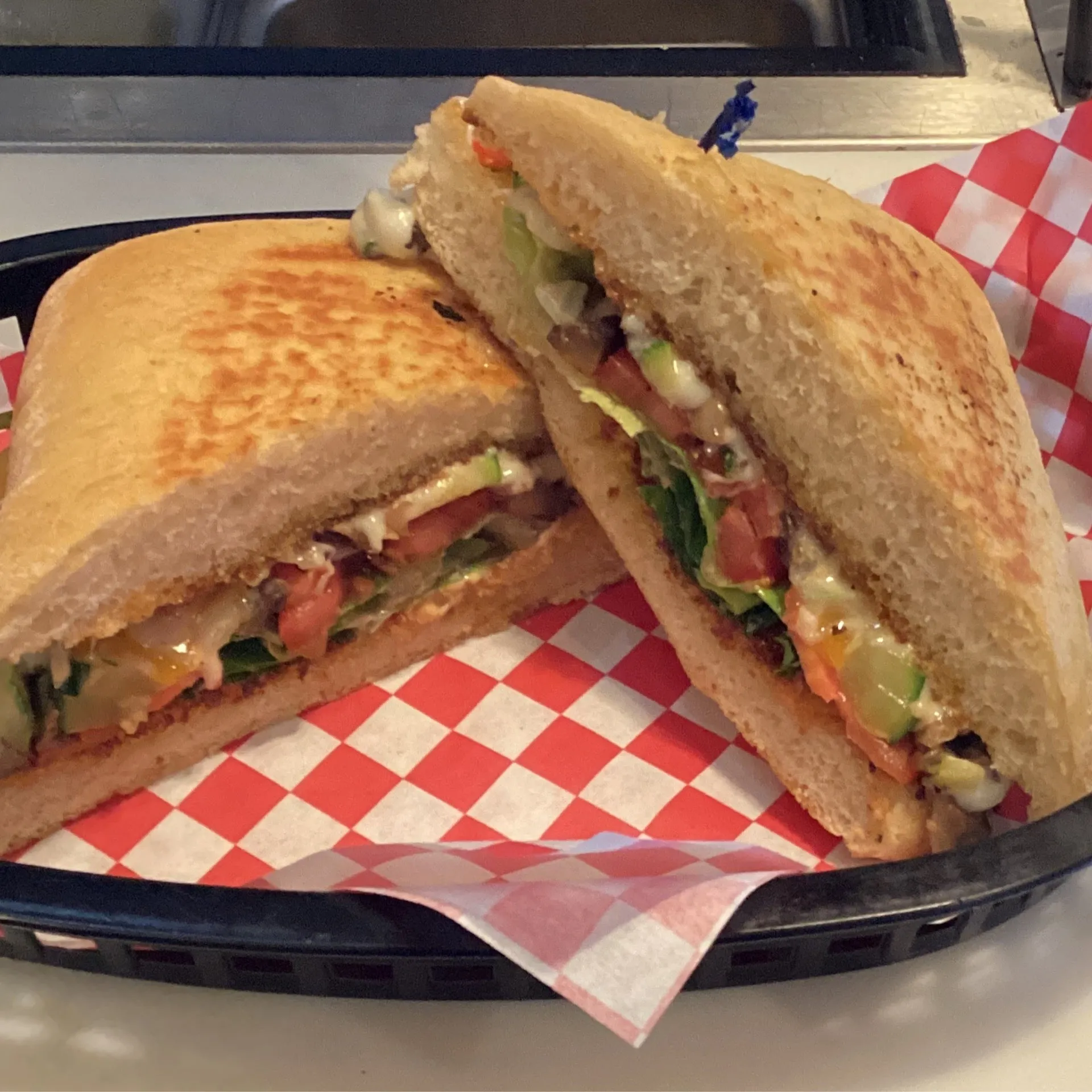 Grilled veggie sandwich with tomato and greens in a deli basket