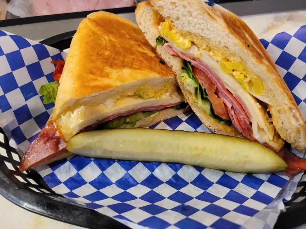 Italian sub with salami, cheese, and a pickle on blue-checkered paper