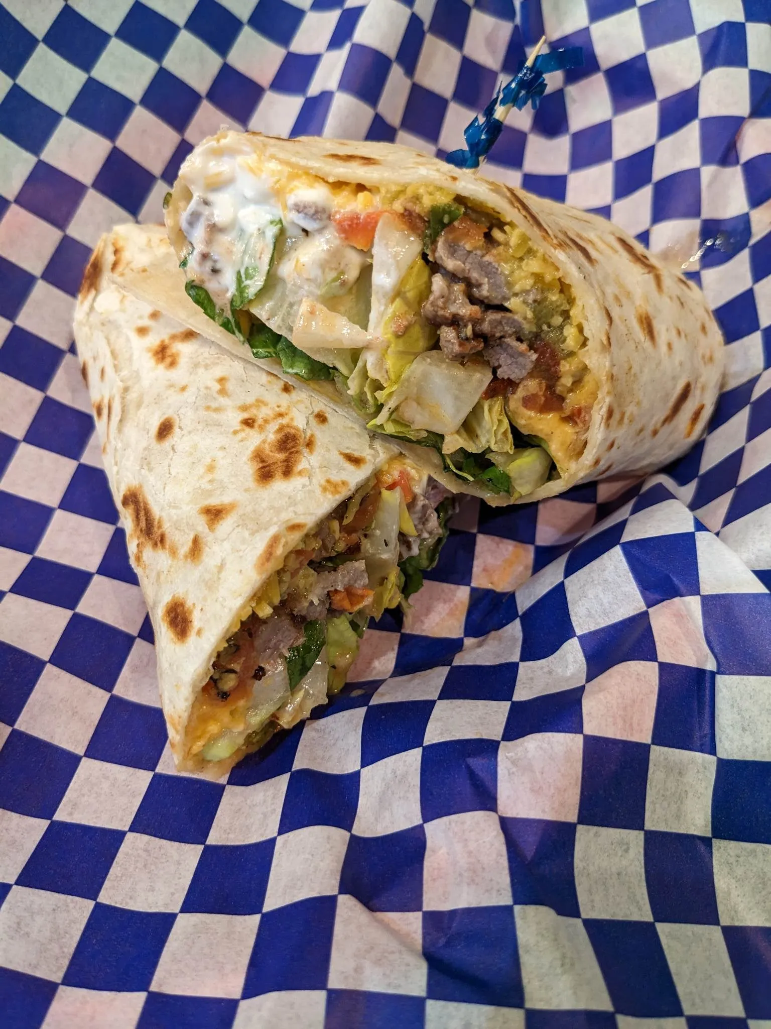 Halved burrito with meat, lettuce, and cheese on blue-checkered paper